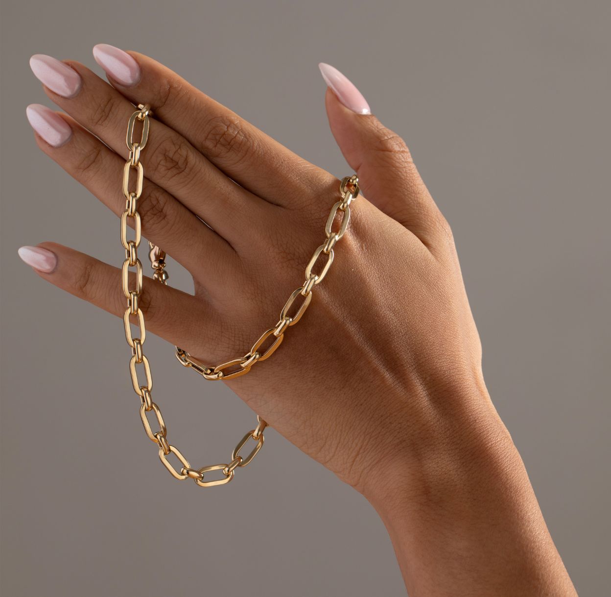 Hand wearing a gold chain bracelet on a plain background