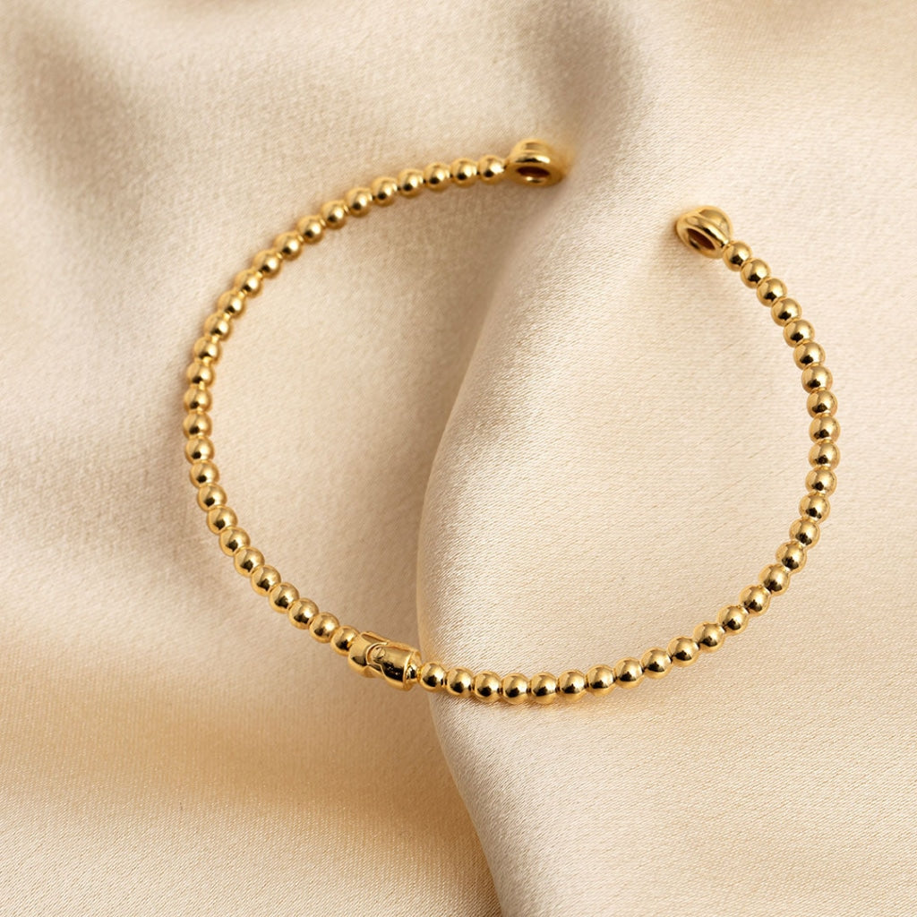 A luxurious gold bead bangle bracelet, featuring a sequence of shiny, spherical gold beads linked together to form a full circle