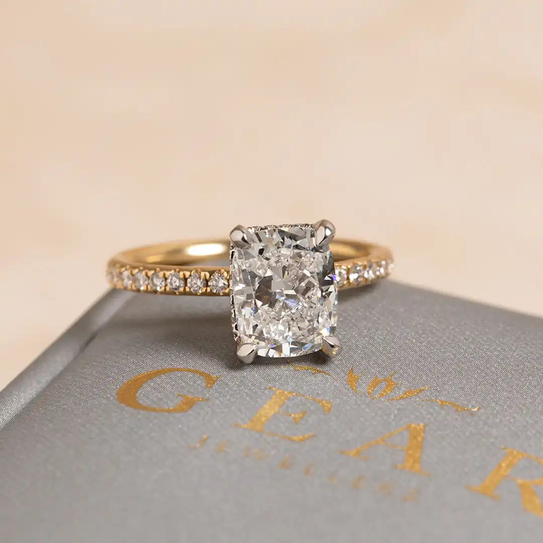 Cushion-cut diamond engagement ring with a gold band featuring small pavé diamonds.