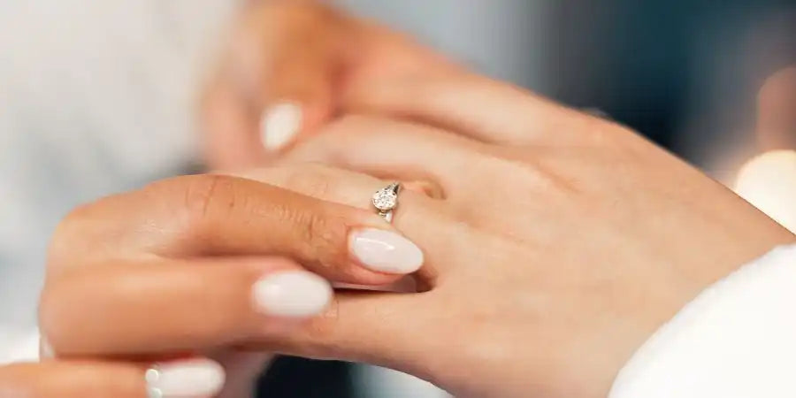 Diamond engagement ring on a hand with pale pink nail polish.