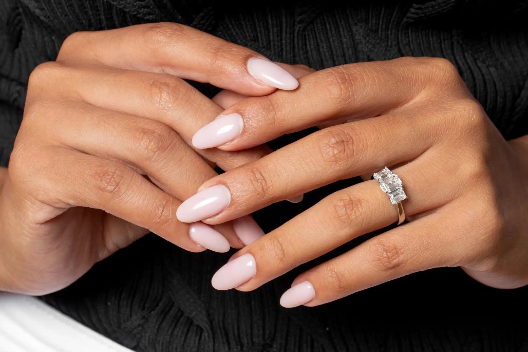 Hands with pale pink manicured nails and a diamond engagement ring.