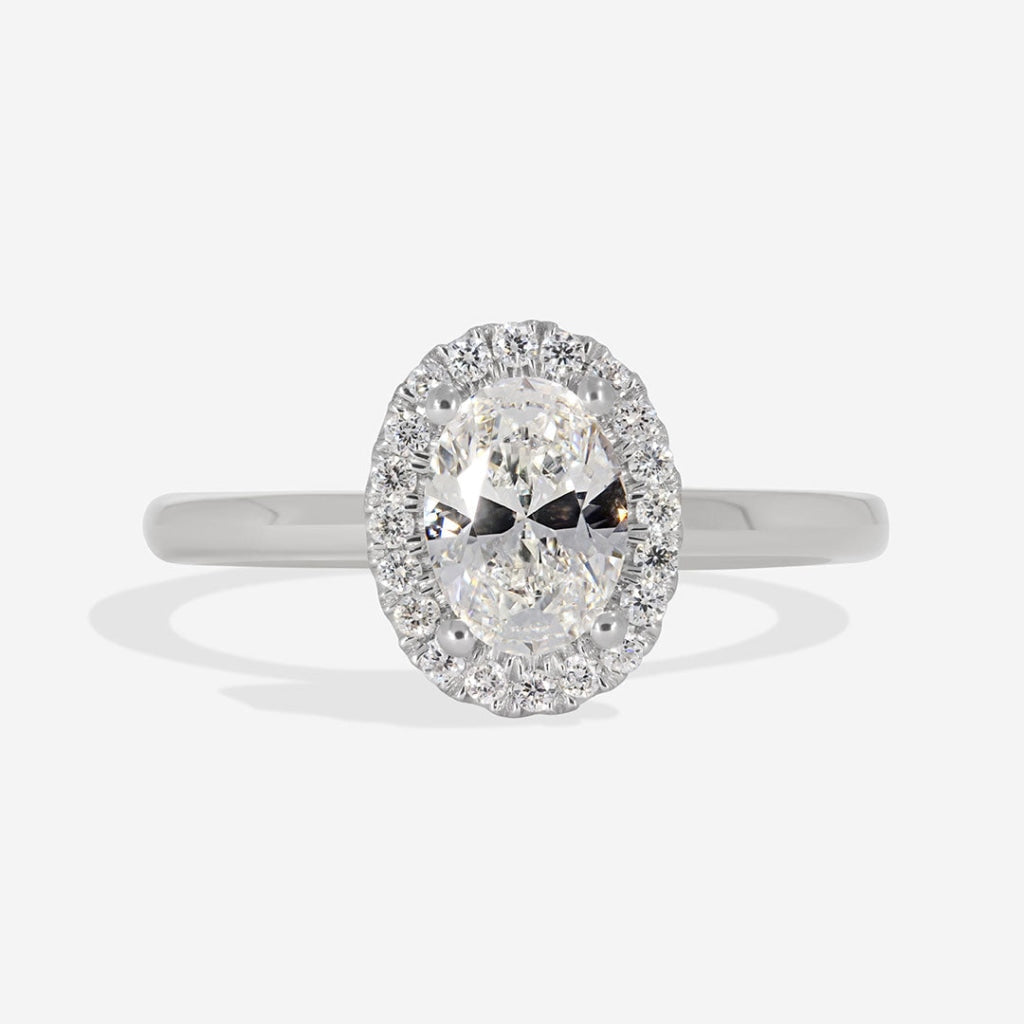 Oval diamond engagement ring with a diamond halo and plain white gold band.