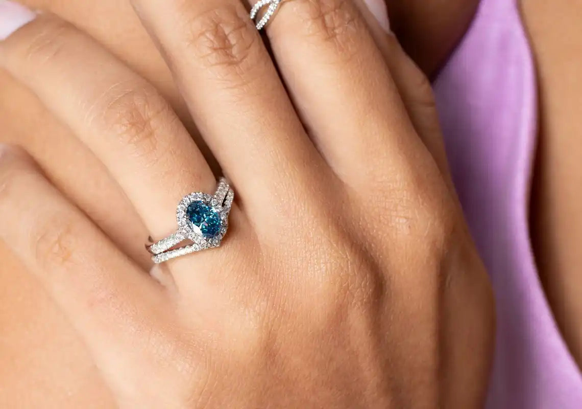 Silver ring featuring a blue gemstone surrounded by small diamonds in a halo setting.
