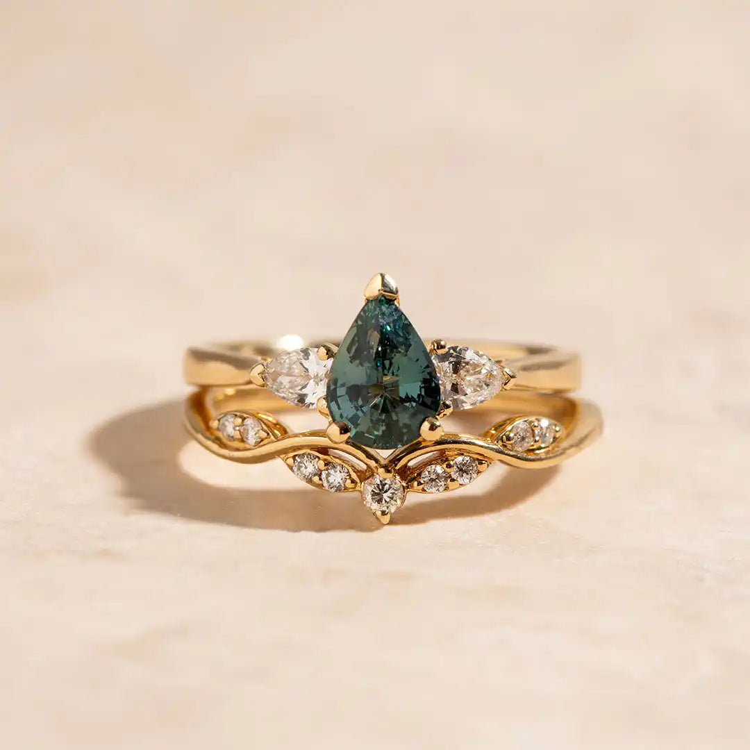 Teardrop-shaped teal sapphire ring with diamond accents set in gold.