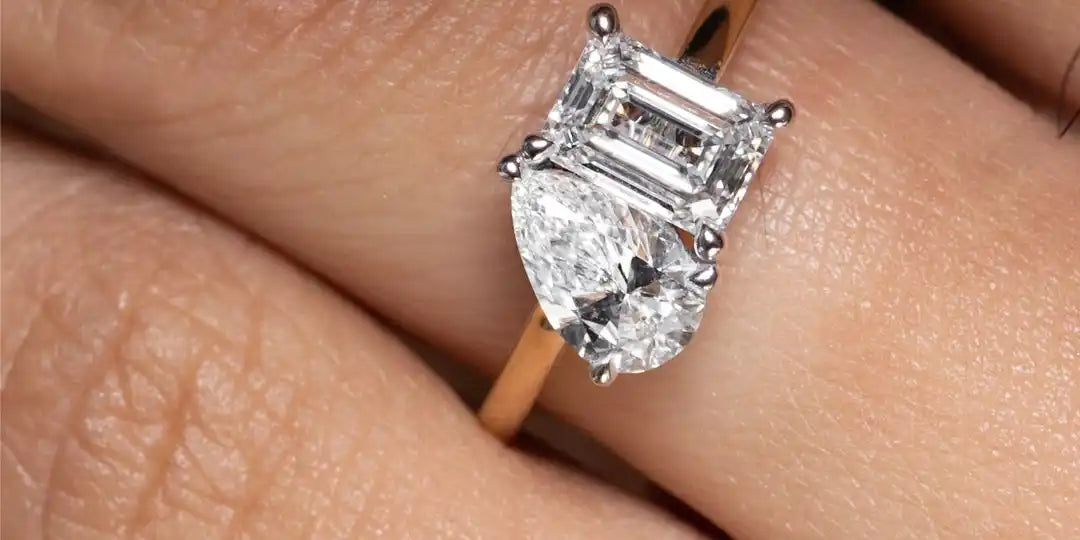 Three-stone engagement ring featuring an emerald-cut center diamond flanked by pear-shaped side stones in a yellow gold band.