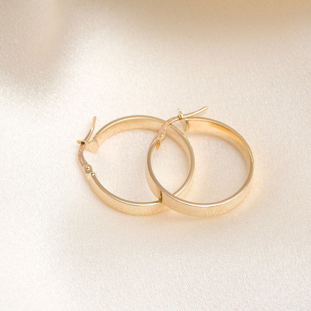 14ct yellow gold hoop earrings on a cream fabric background