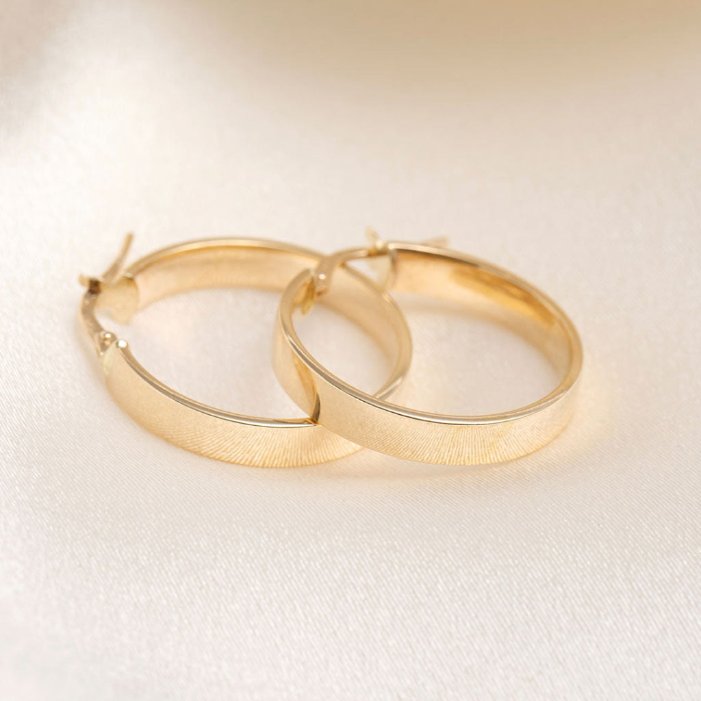 14ct yellow gold hoop earrings on a cream fabric background