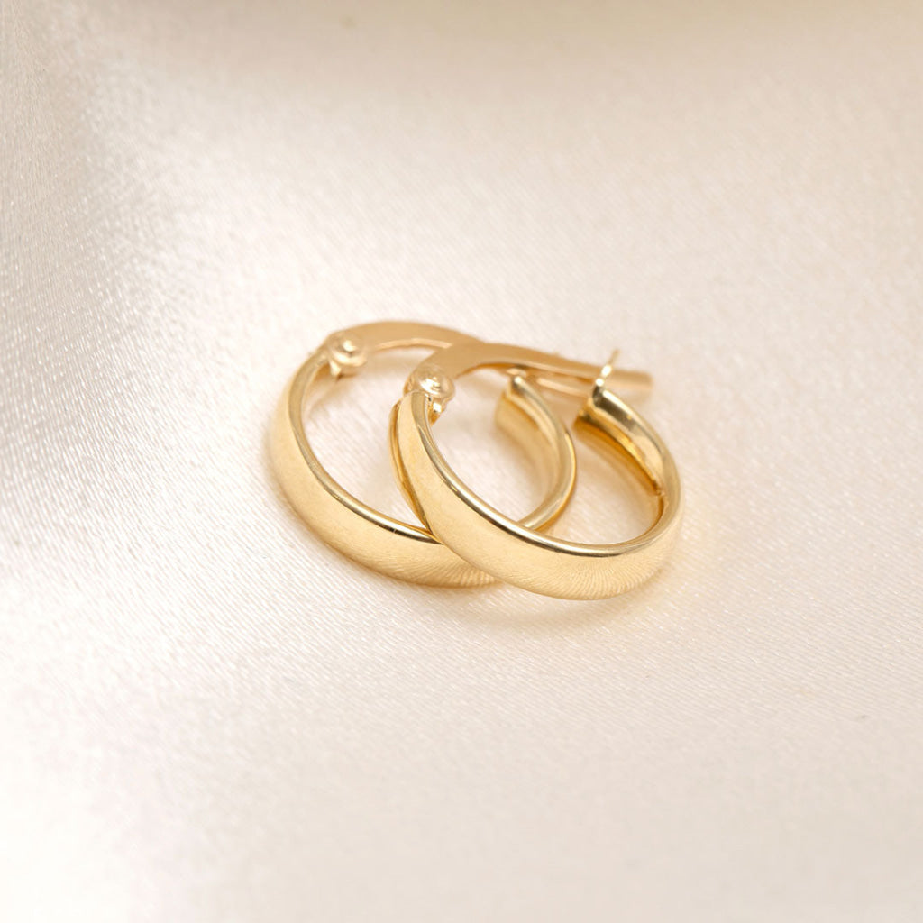 18ct gold hoop earrings on cream fabric background