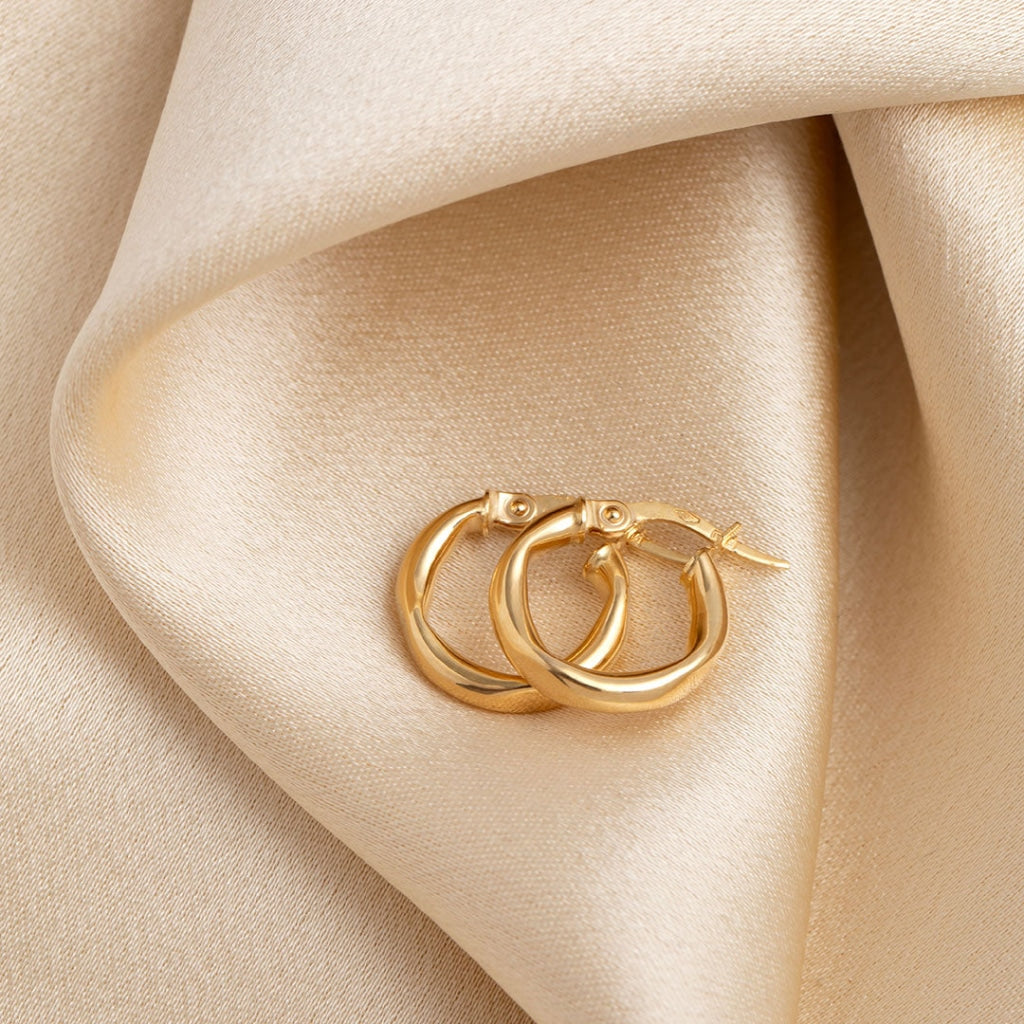 Double hoop gold earrings resting on a creamy beige fabric, showcasing their polished finish and intertwined design for a touch of elegance