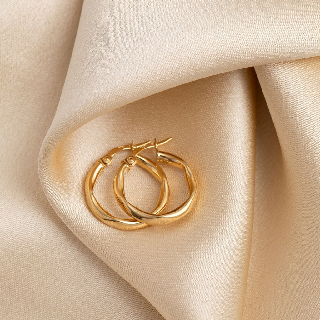 Double hoop gold earrings resting on a creamy beige fabric, showcasing their polished finish and intertwined design for a touch of elegance