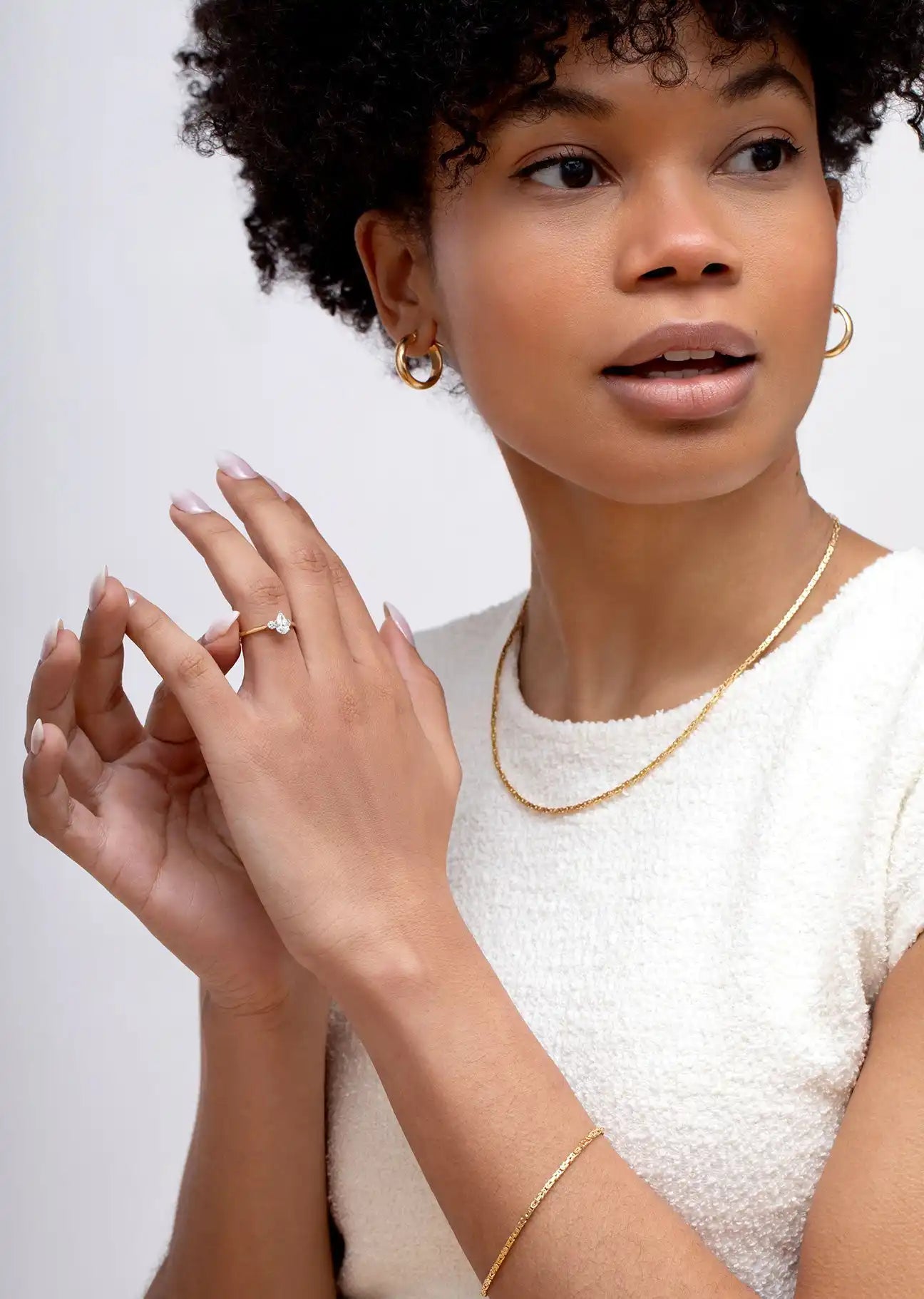 A delicate gold chain bracelet worn with a white textured top.