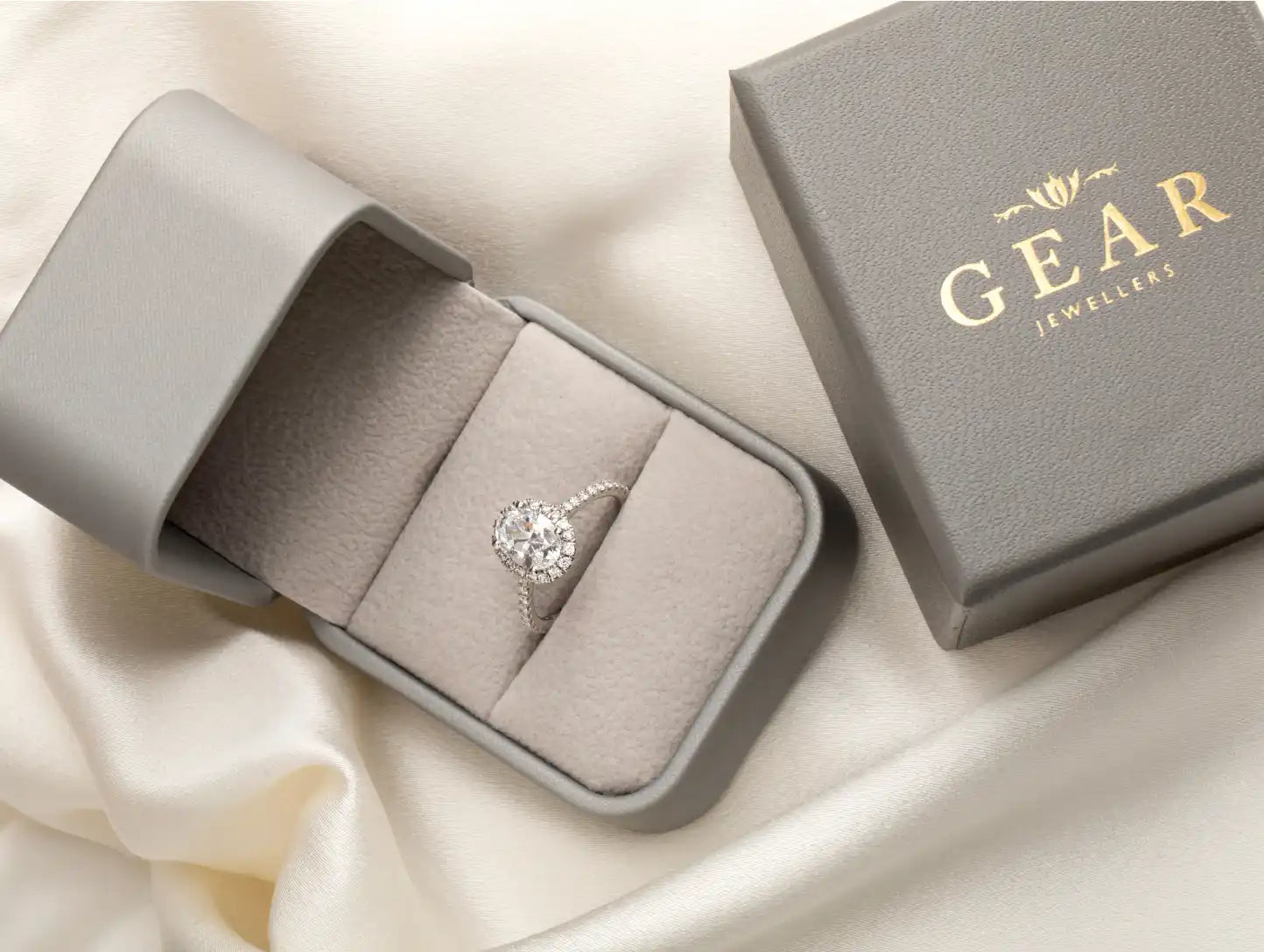 A diamond engagement ring nestled in a gray velvet ring box with ’GEAR’ branding.