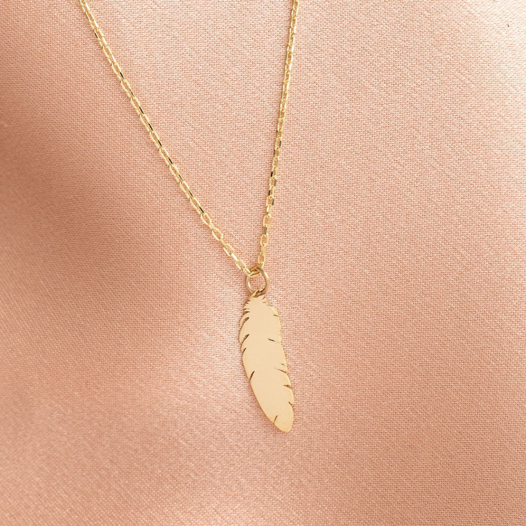9ct gold feather necklace beside a purple ribbon