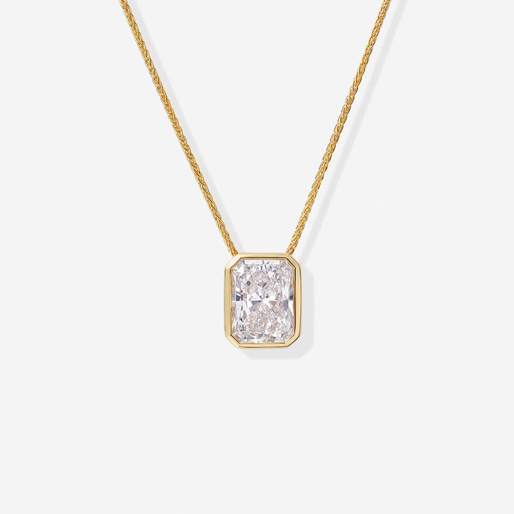 A yellow gold necklace featuring a radiant cut diamond pendant in a gold bezel setting.
