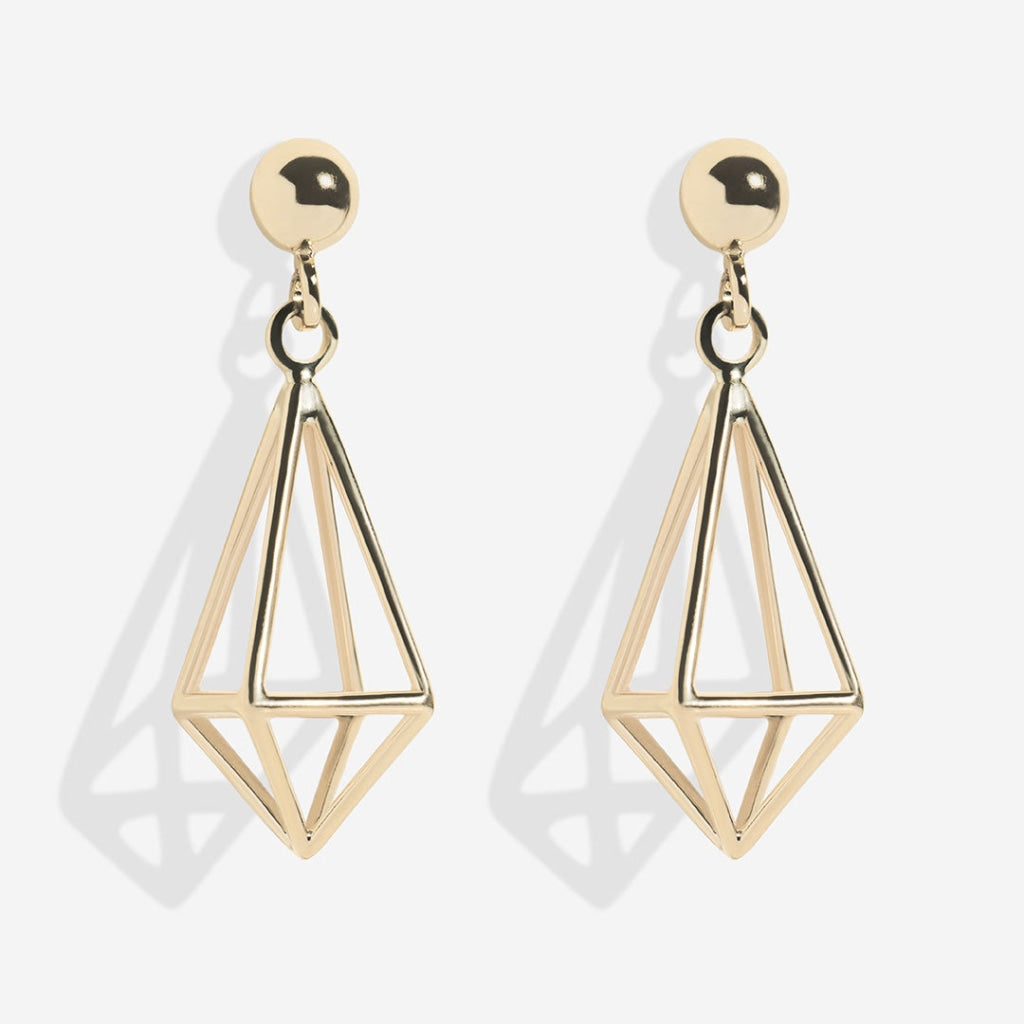 Gold geometric earrings with a shiny spherical stud on top and an open triangular prism-shaped dangle, casting a soft shadow on a white background
