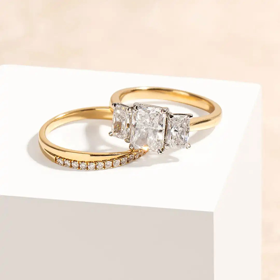 Gold wedding ring set featuring three princess-cut diamonds and a matching pavé band.