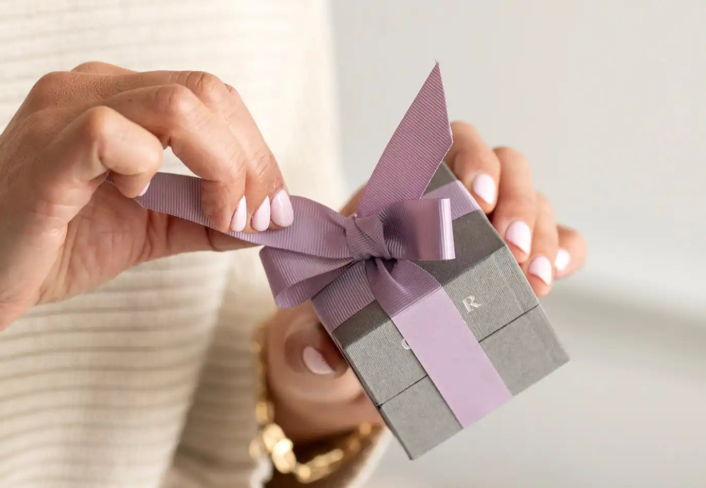 Gray gift box with a lavender ribbon tied in a bow.