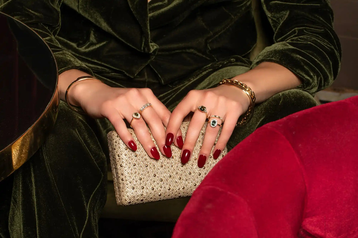 Hands with red manicured nails rest on a sparkly beaded clutch purse.