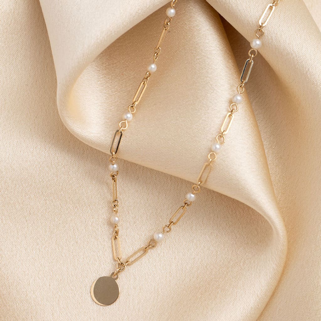 Gold chain necklace with evenly spaced pearls leading to a central disc charm