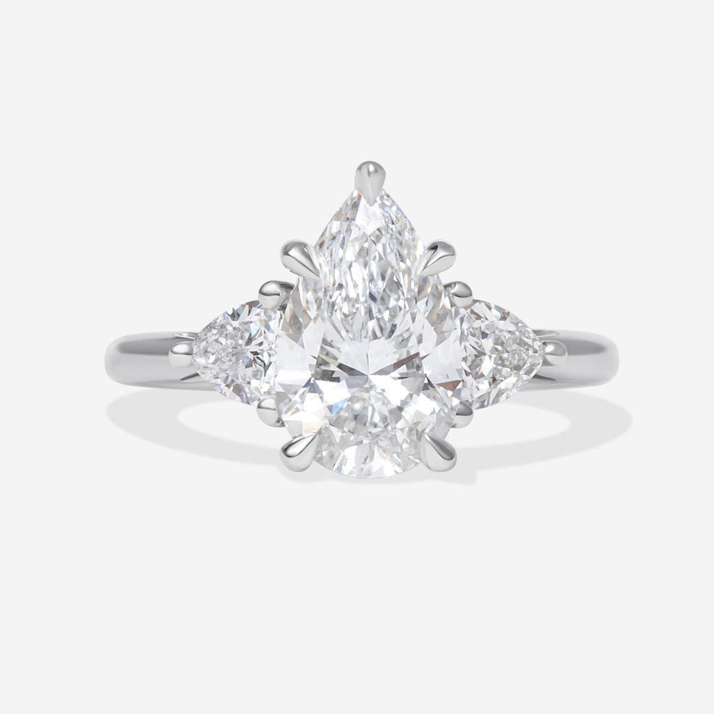 A platinum ring featuring a pear-cut center diamond flanked by two trillion cut lab-grown diamonds, displayed on a white background.