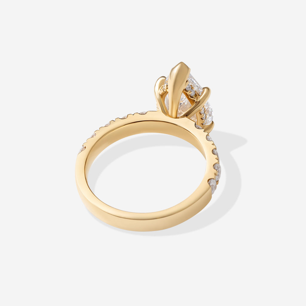The shank view of a yellow gold ring featuring a large pear-cut clear center stone and smaller round stones along the band.