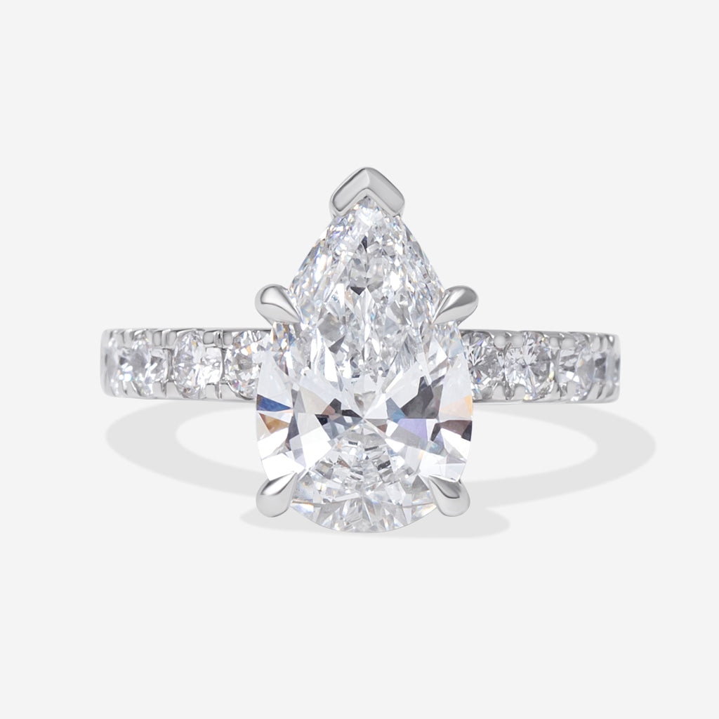A pear-cut diamond engagement ring with a pavé band set in platinum metal, shown on a light gray background.