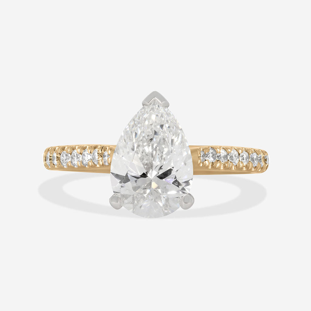 A pear-cut diamond engagement ring with a yellow gold band accented by pavé diamonds, shown on a light gray background.