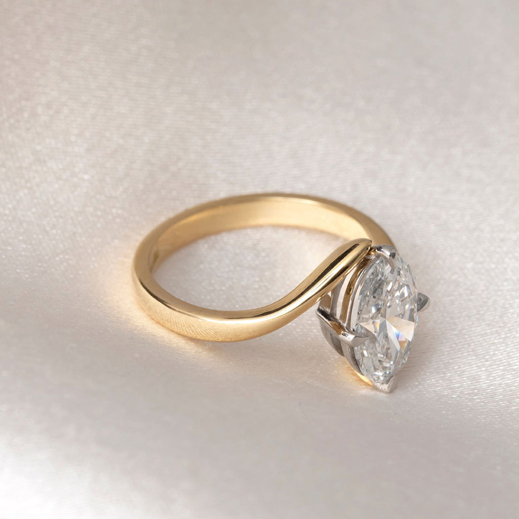 An oval cut lab grown diamond engagement ring, displayed on draped cream satin fabric.