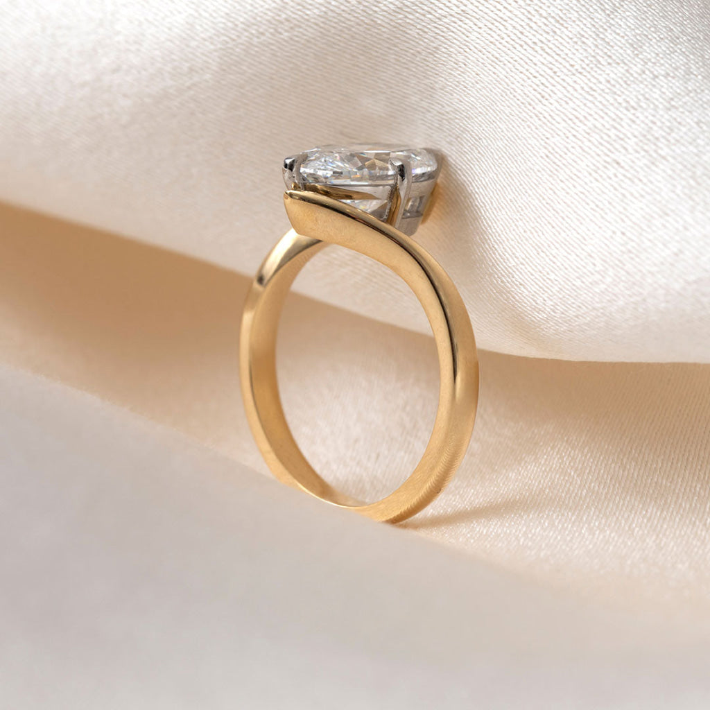 An oval cut lab grown diamond engagement ring, displayed on draped cream satin fabric.