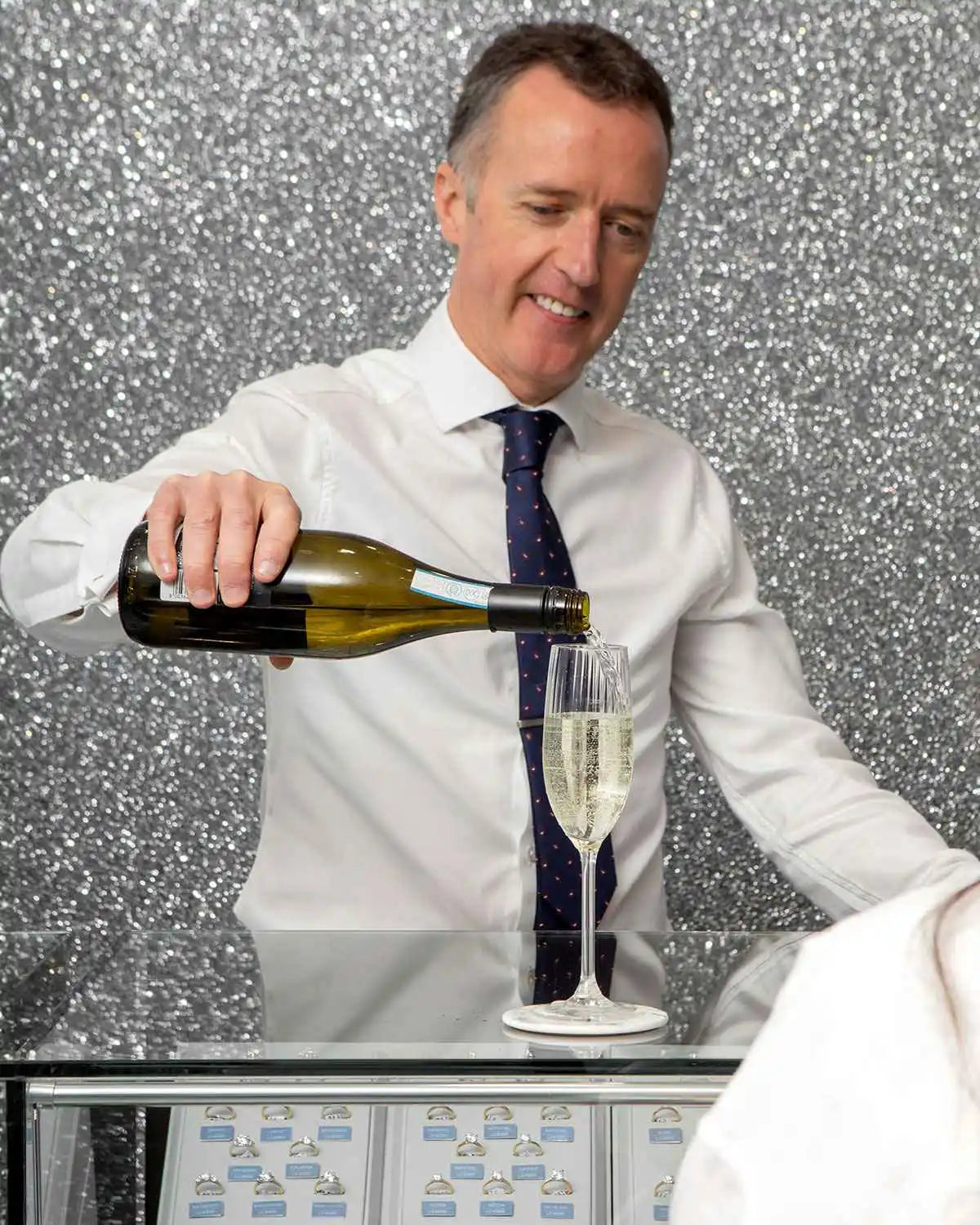 A person in business attire pouring champagne into a glass.