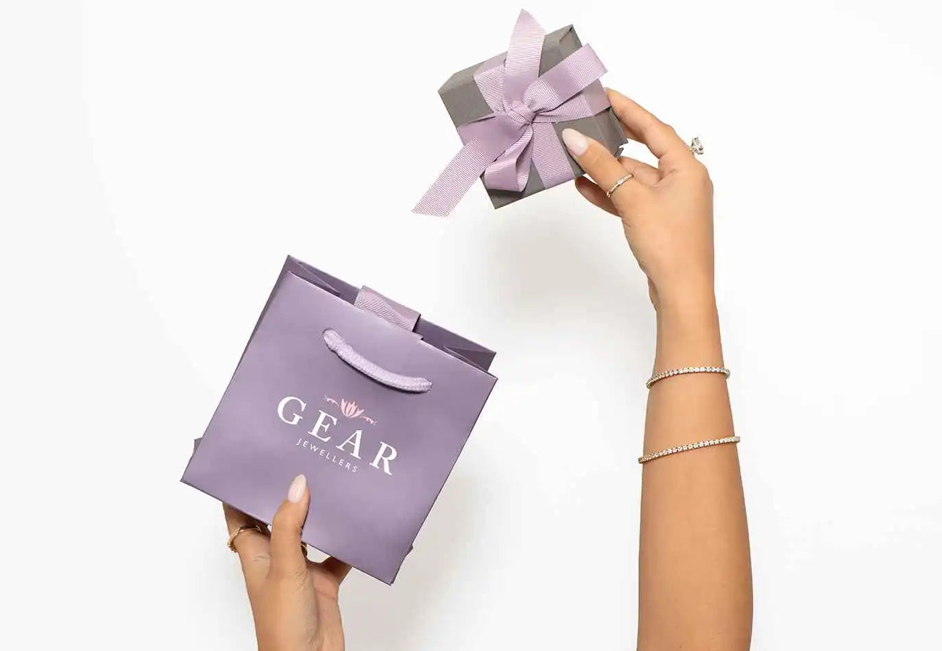 Purple gift bag with ’GEAR’ text and a matching bow being held.