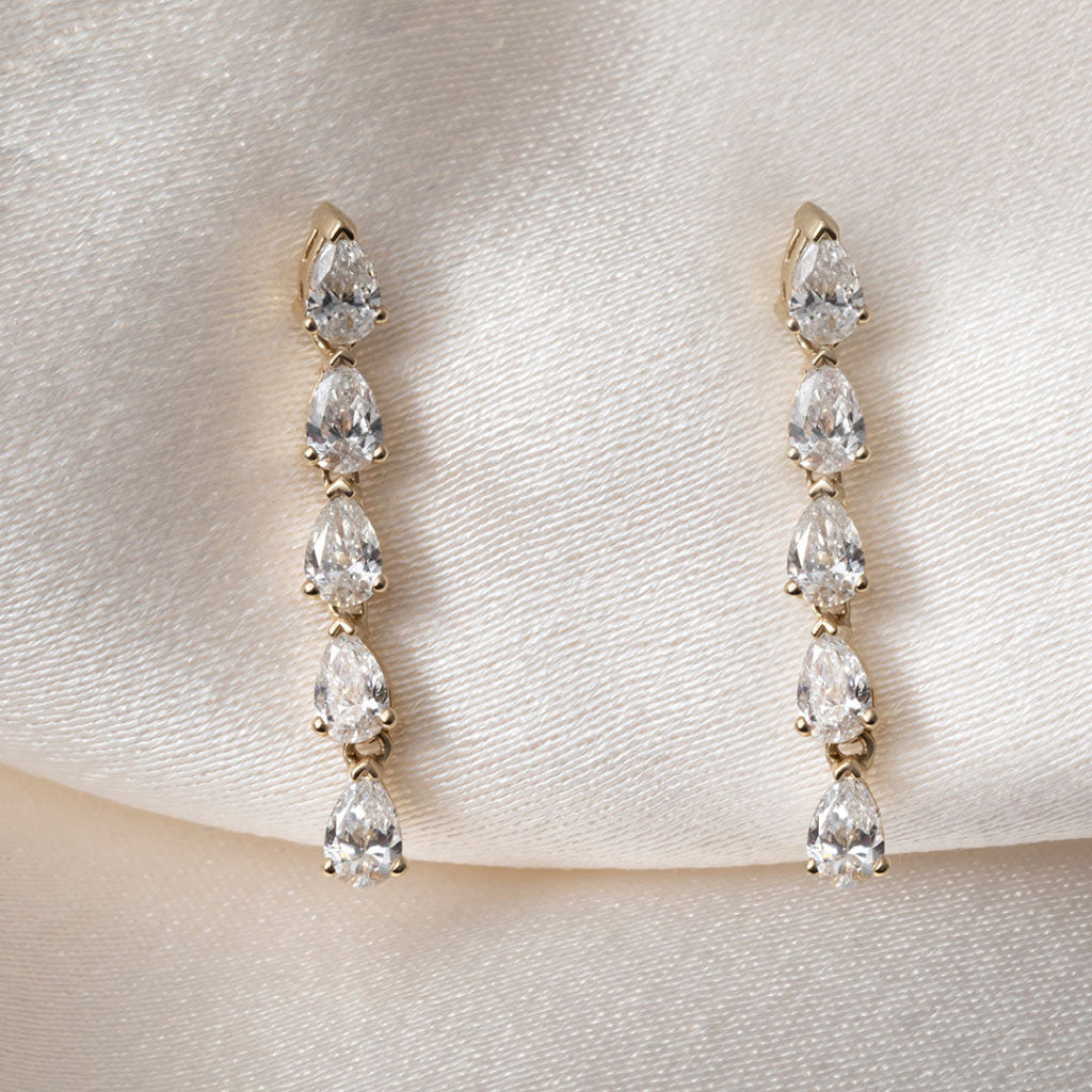 A pair of gold drop earrings featuring a vertical arrangement of five pear-cut diamonds in a claw setting.
