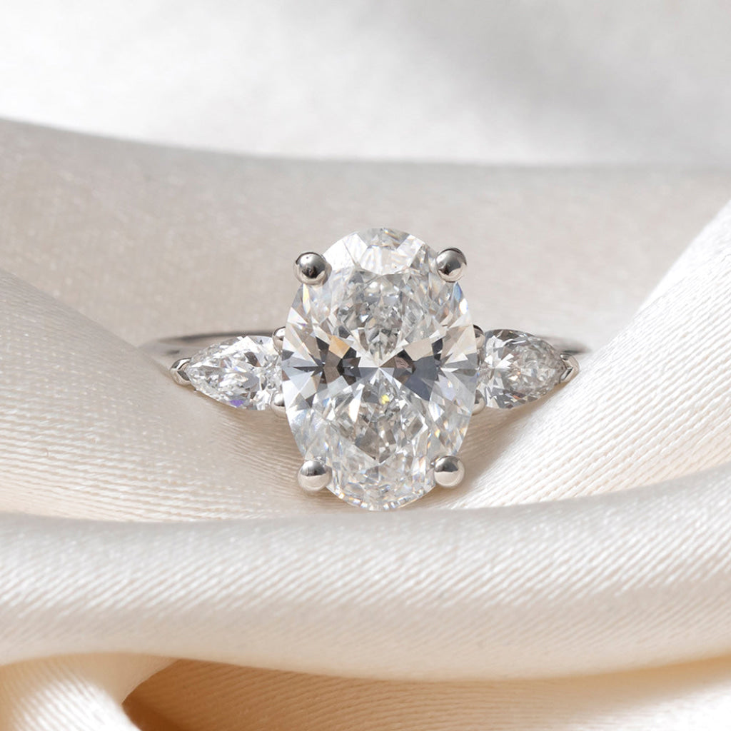 An oval diamond engagement ring with a platinum band featuring small pear-cut side diamonds.