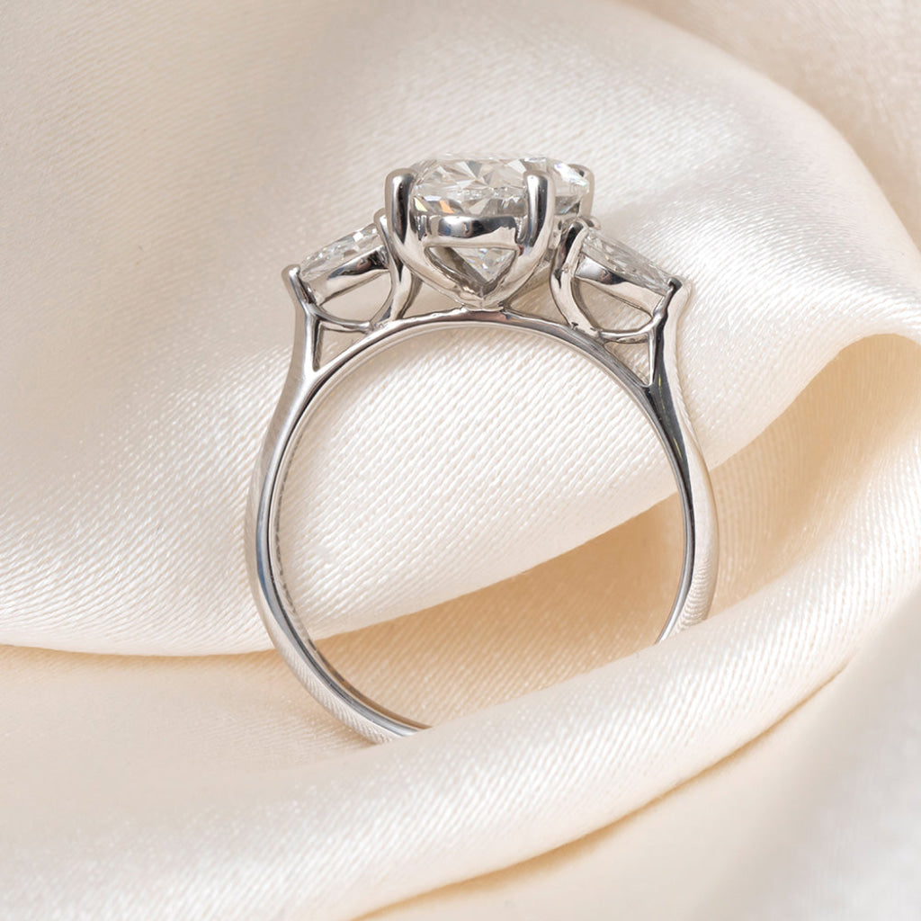 An oval diamond engagement ring with a platinum band featuring small pear-cut side diamonds.
