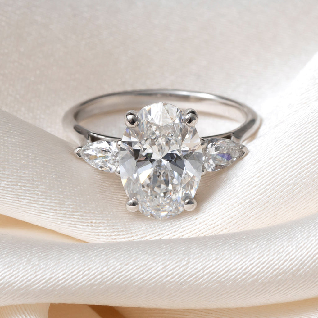 An oval diamond engagement ring with a platinum band featuring small pear-cut side diamonds.