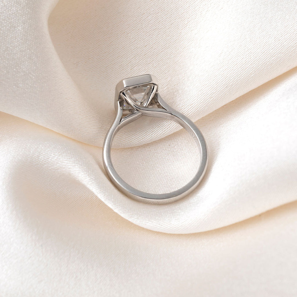An emerald-cut diamond ring in a platinum band, resting on a soft, textured white fabric background.