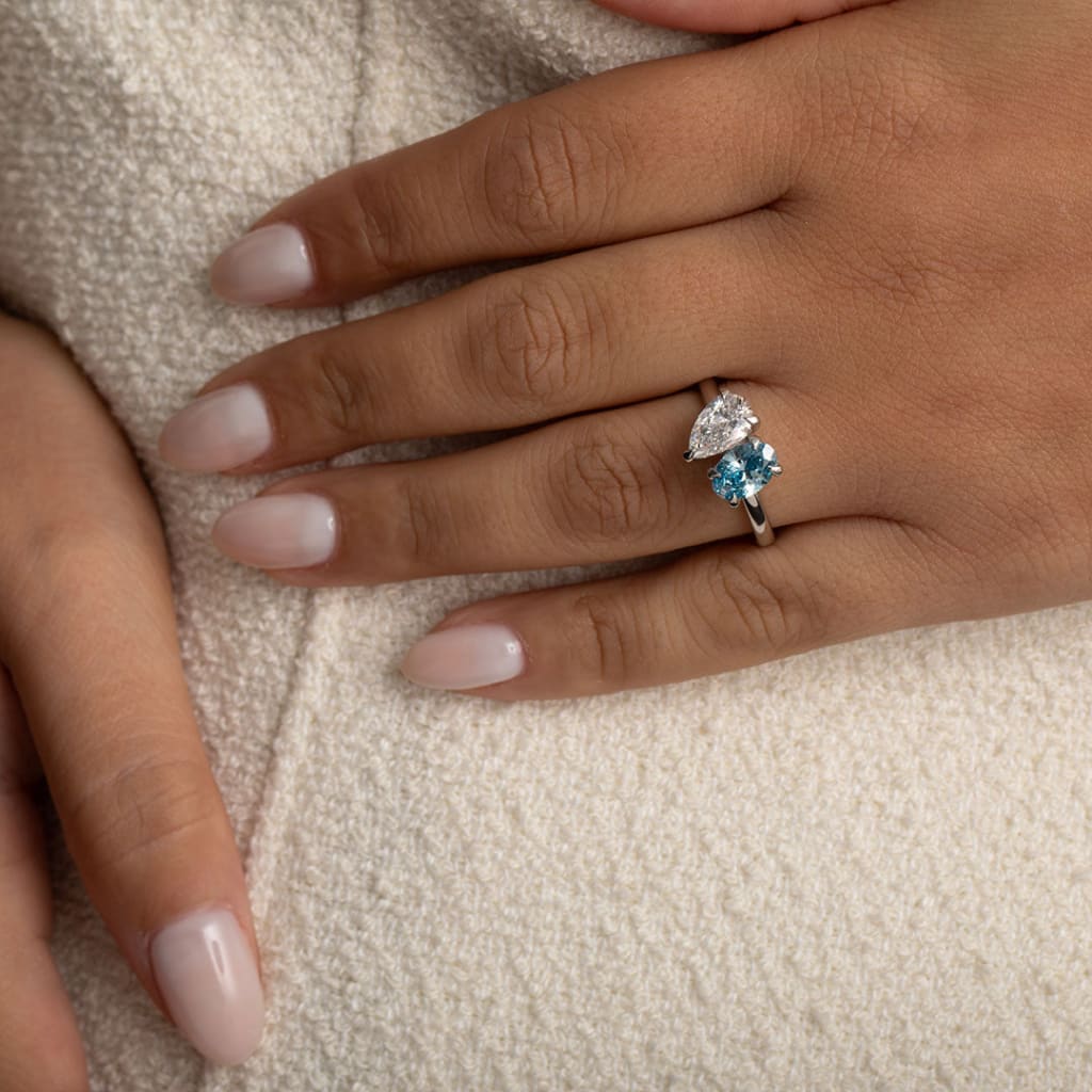 hand shot of blue oval and pear cut engagement ring in platinum