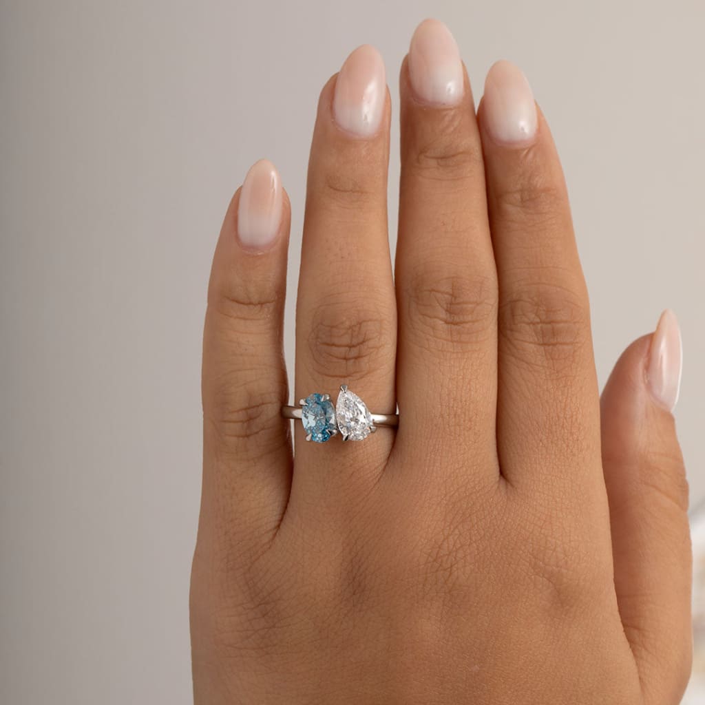 close up of vivid blue and lab grown pear cut engagement ring on models hand