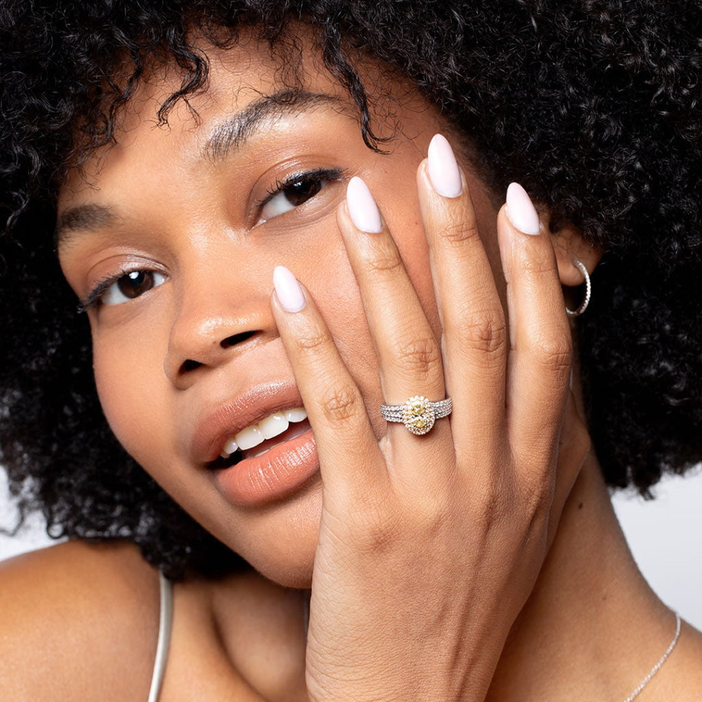 Model smiling with hand on face wearing yellow diamond engagement ring