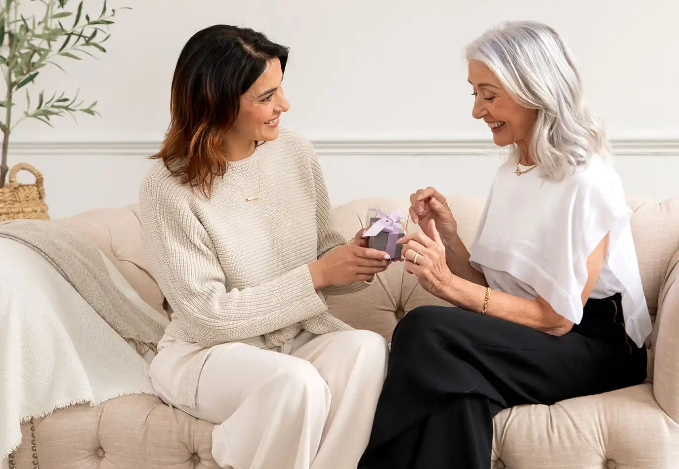 Two people sitting on a couch exchanging a gift or small package.