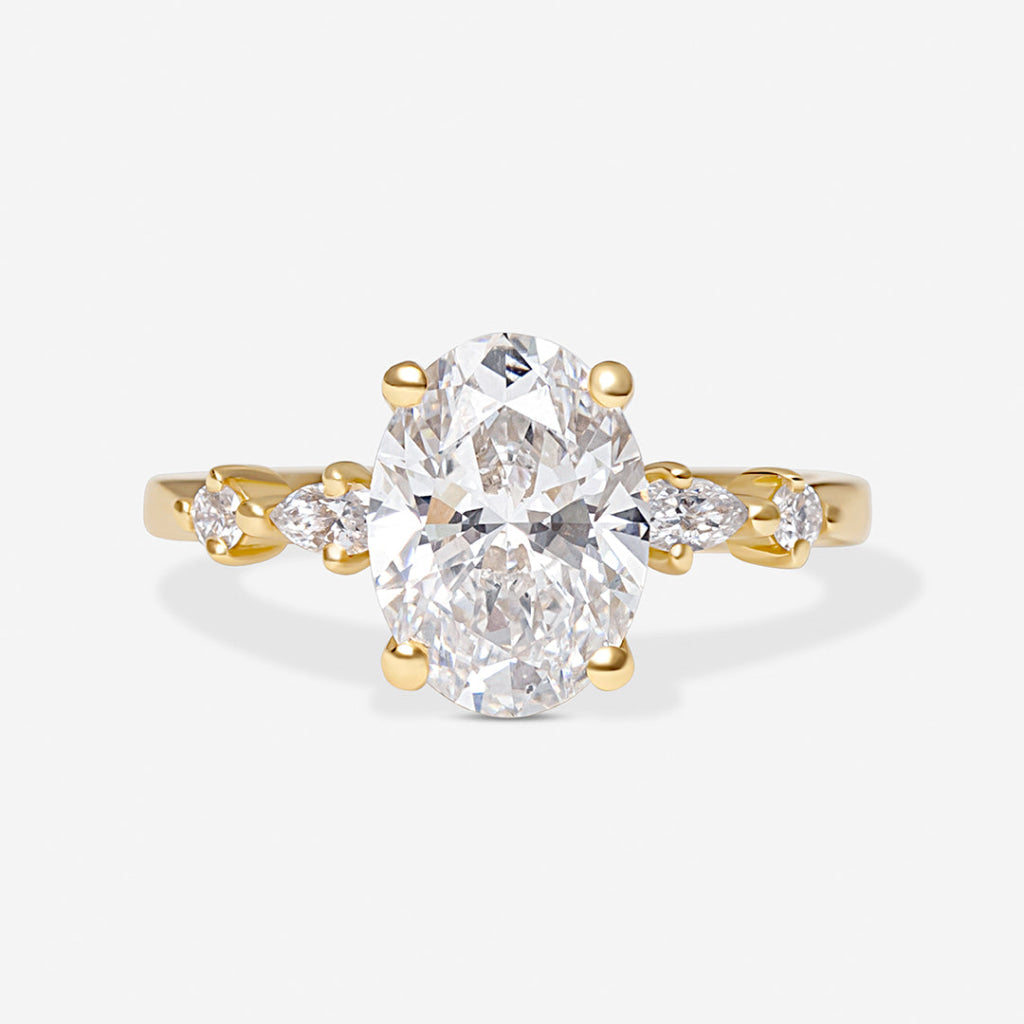 A yellow gold solitaire-style ring featuring a large oval-cut clear center stone with smaller marquise-cut side stones on a light gray background.