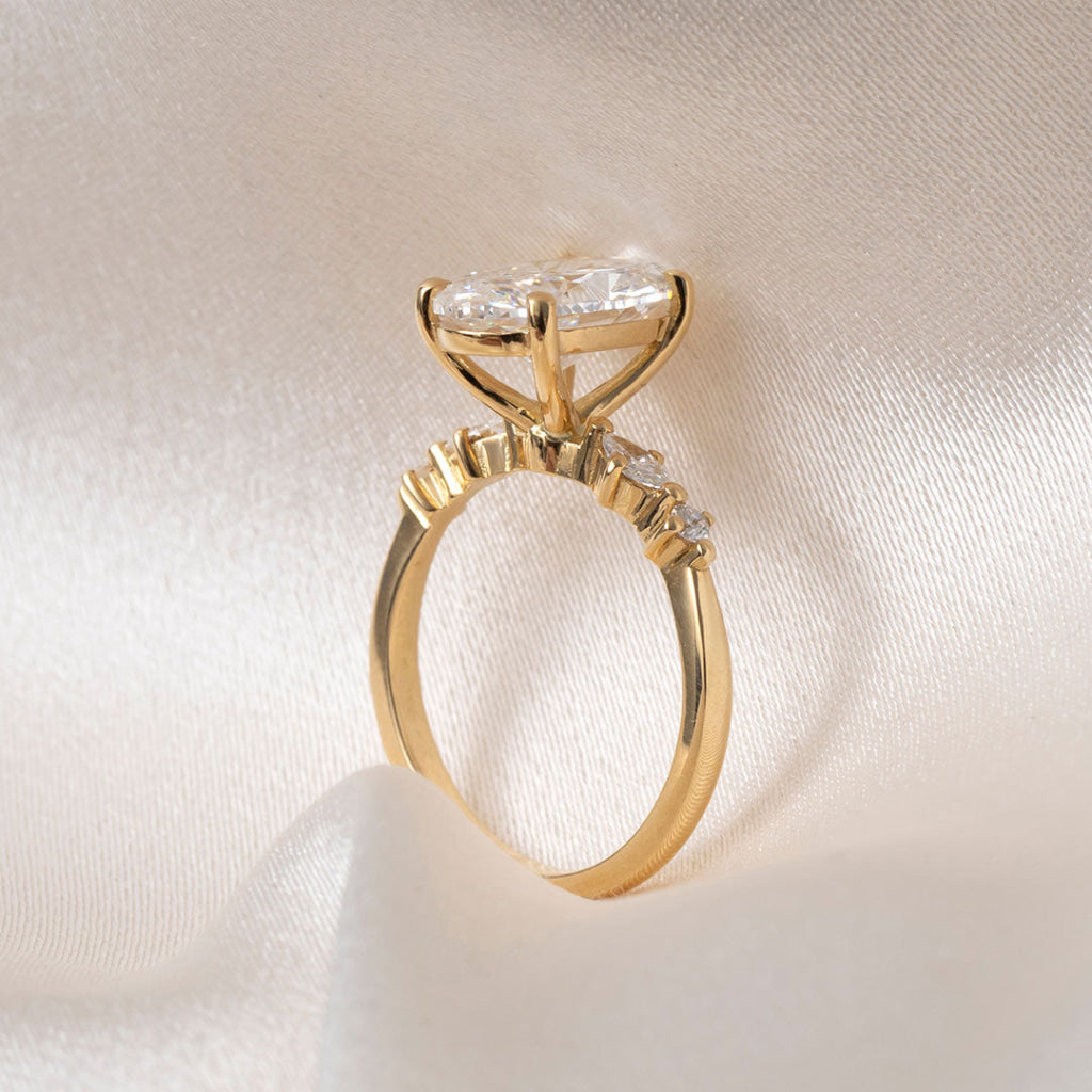 An oval diamond engagement ring with a yellow gold band, resting on draped cream-colored satin fabric.